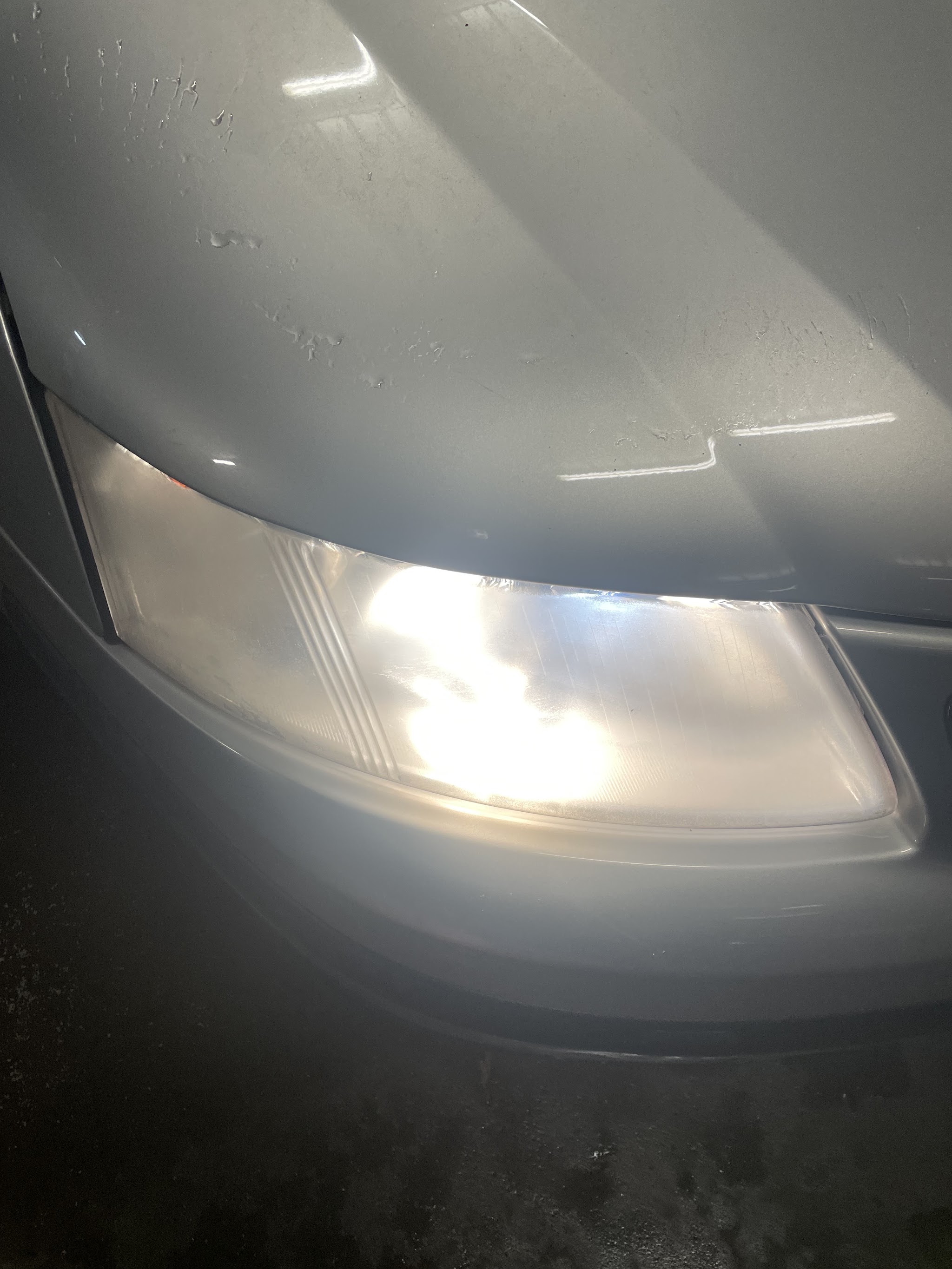 Headlight on a customer's silver car photographed in the workshop